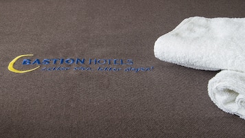 Una coperta marrone con un logo e del testo per Bastion Hotels, e un asciugamano bianco piegato sul lato destro.