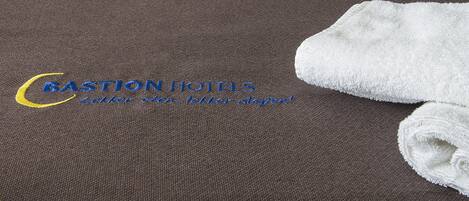 A brown bedspread with a logo and text for Bastion Hotels, and a folded white towel on the right side.