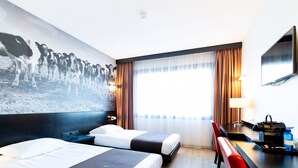 Habitación de hotel con dos camas, un escritorio, una silla, un televisor y un cuadro grande en la pared.