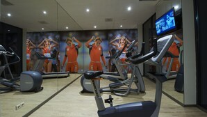 Un gimnasio con varias cintas de correr, bicicletas estáticas y un espejo con imágenes deportivas.