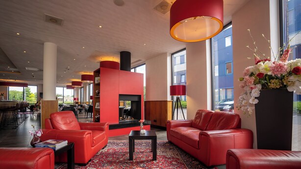 Un hall amplio con sofás de cuero rojo, una alfombra estampada y un gran ventanal con vistas al exterior.