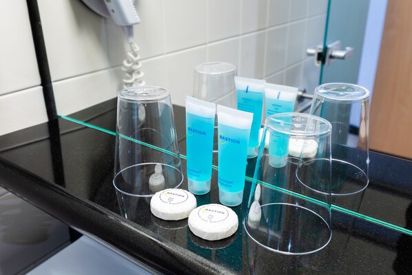Una encimera de baño con diversos artículos de aseo, como botellas y recipientes, probablemente en un hotel.
