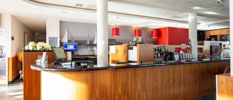A modern hotel reception area with a wooden reception desk, a digital screen, and a red accent wall.