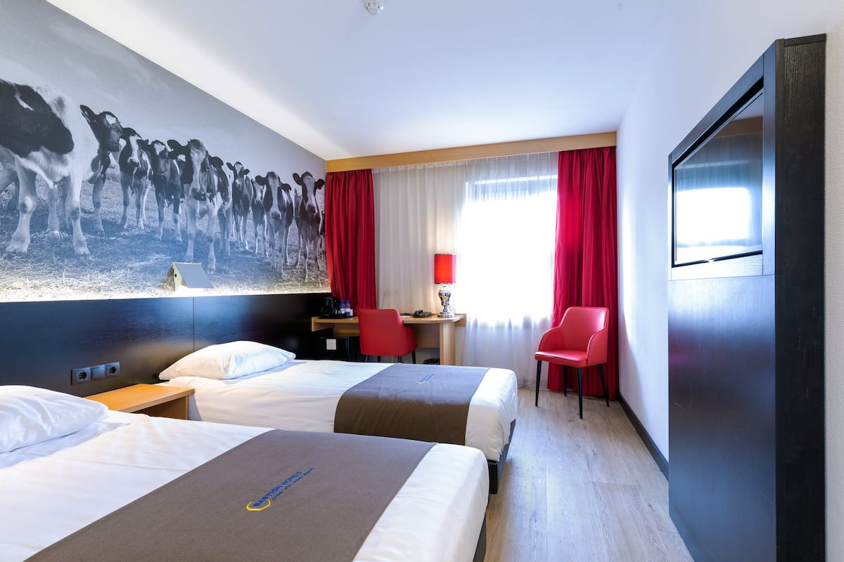 A hotel room with two beds, a desk, a chair, a TV, and a large wall mural.