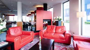 Eine moderne Lobby mit roten Ledersofas, einer zentralen roten Säule und einem großen Fenster mit Blick nach draußen.