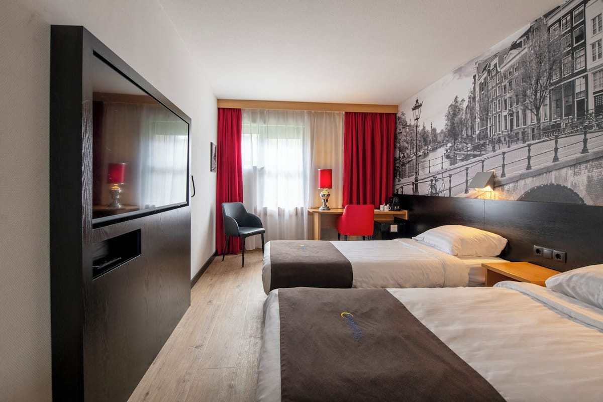 Habitación de hotel con dos camas, un escritorio, una silla y un televisor.