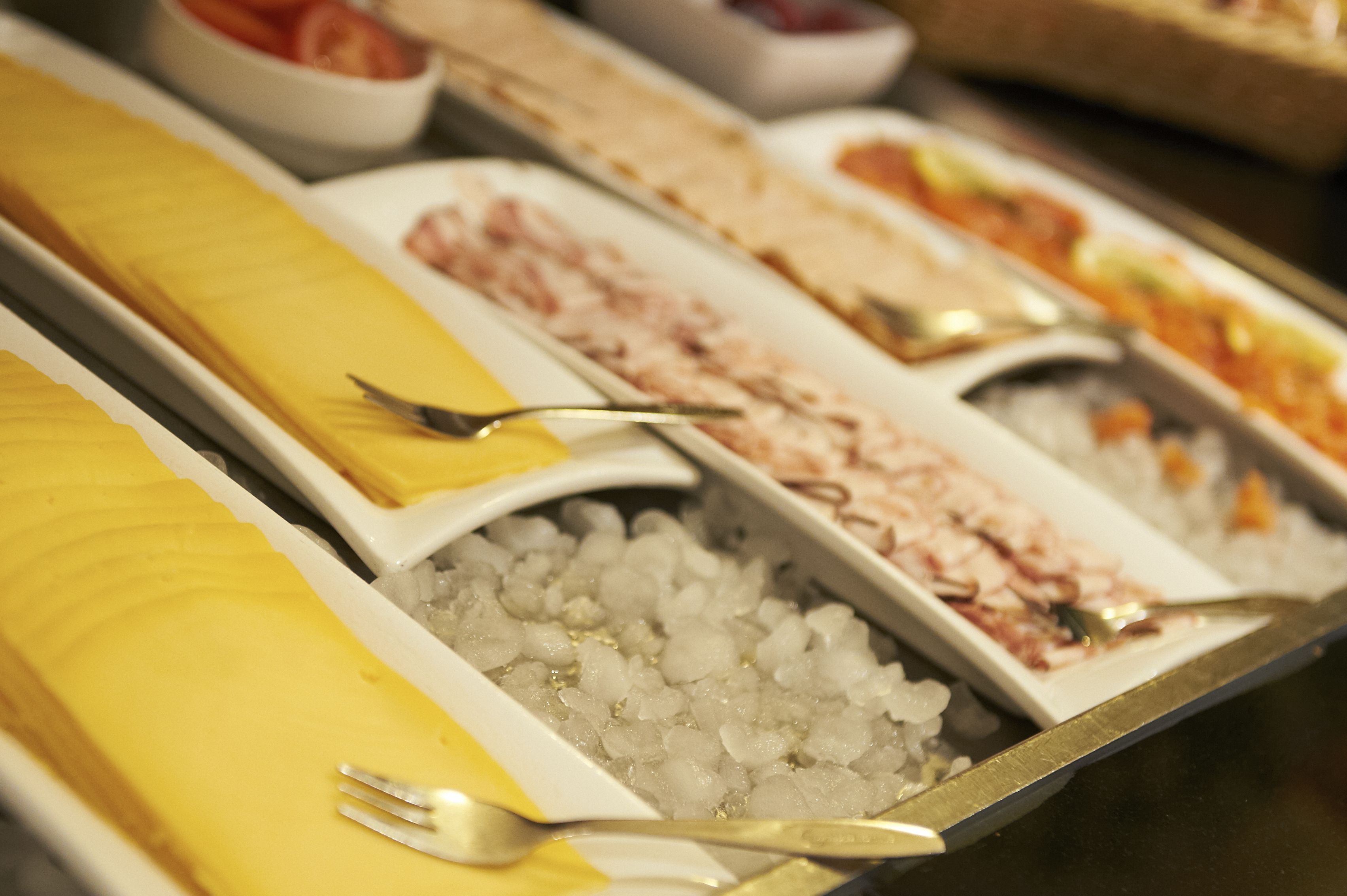 Un bufé con diversos alimentos, incluyendo un plato amarillo, uno blanco con hielo y un plato con una sustancia rosada.