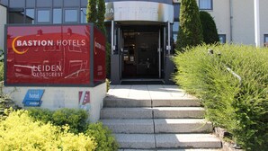 Entrada de hotel con un letrero de Bastion Hotels, una escalera que conduce a la entrada y un asta con una bandera.