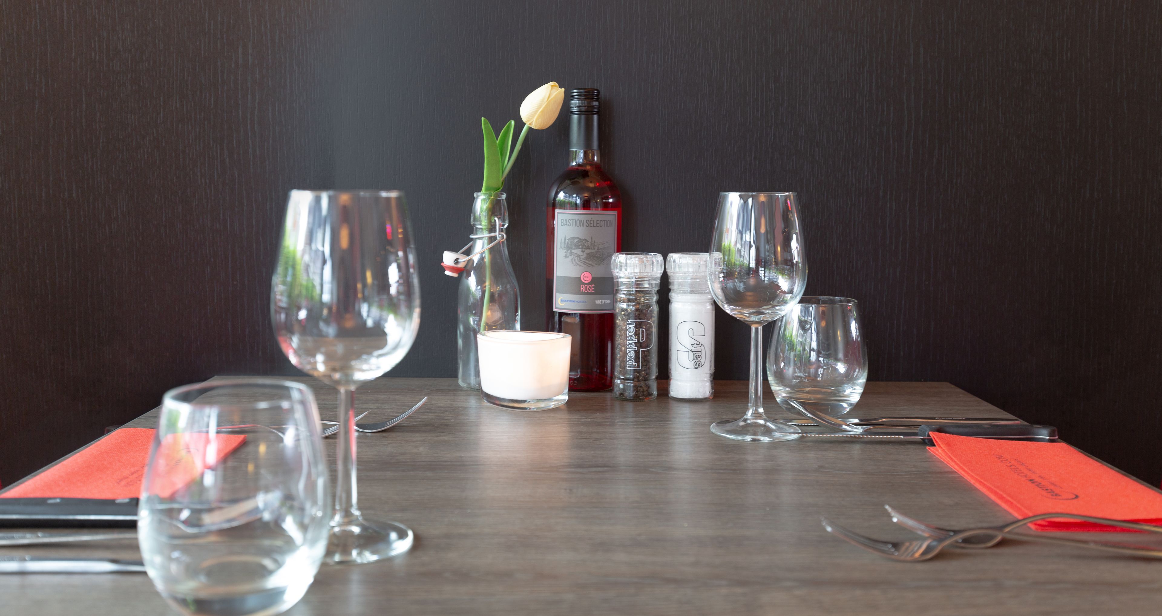 Une table dressée avec des verres à vin, une bouteille de vin, une bougie et des condiments.
