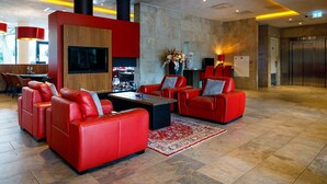 A modern lobby with red leather sofas, a flat-screen TV, a fireplace, and an elevator. - Bastion Hotel Tilburg (Tilburg)