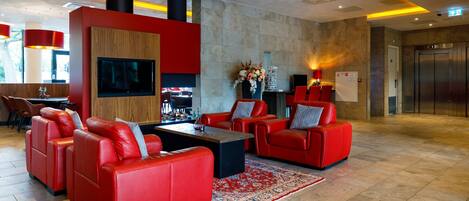 Um lobby moderno com sofás de couro vermelho, uma TV de tela plana, lareira e elevador.