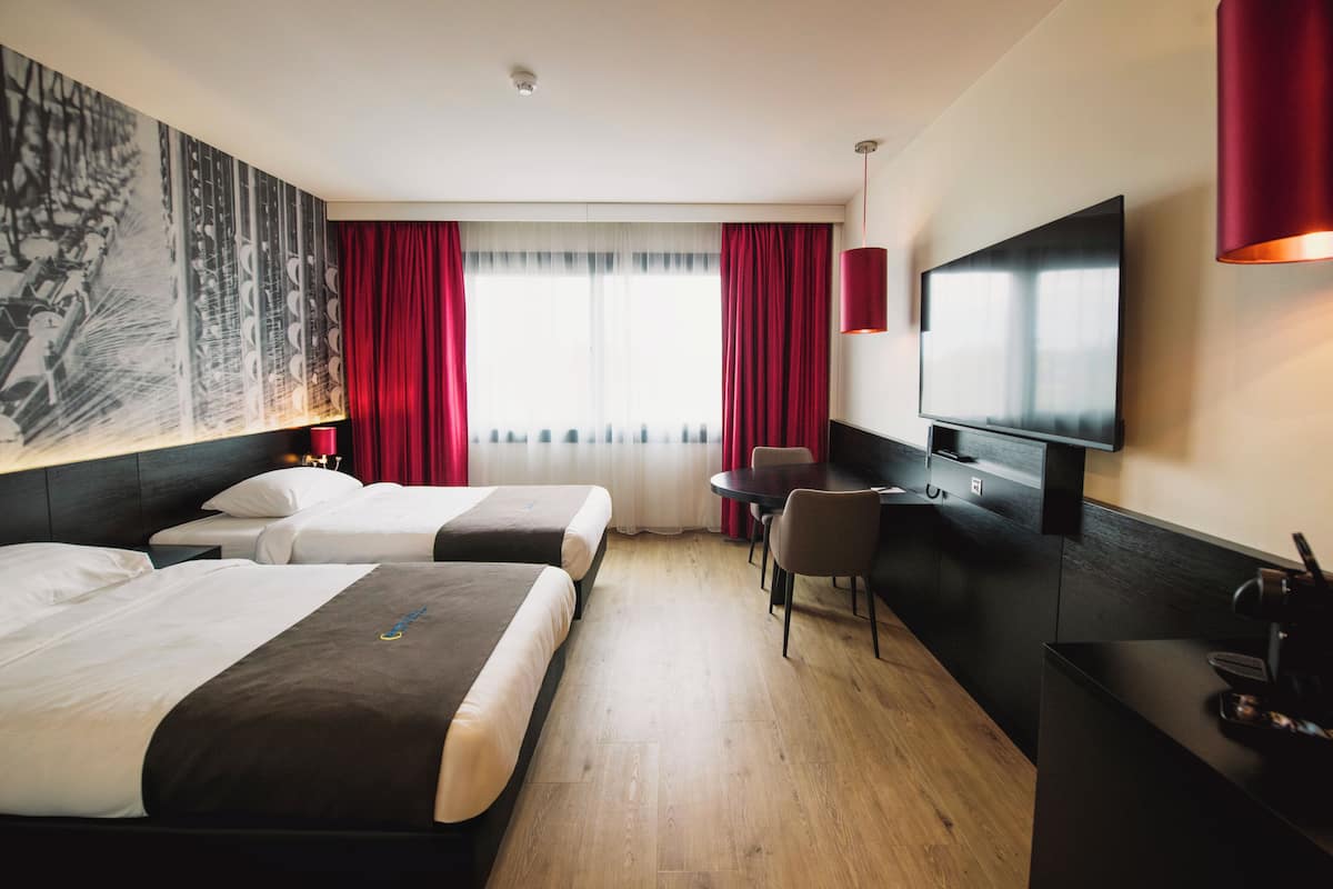 Habitación de hotel con dos camas, un escritorio, una silla, un televisor y un cuadro grande en la pared.