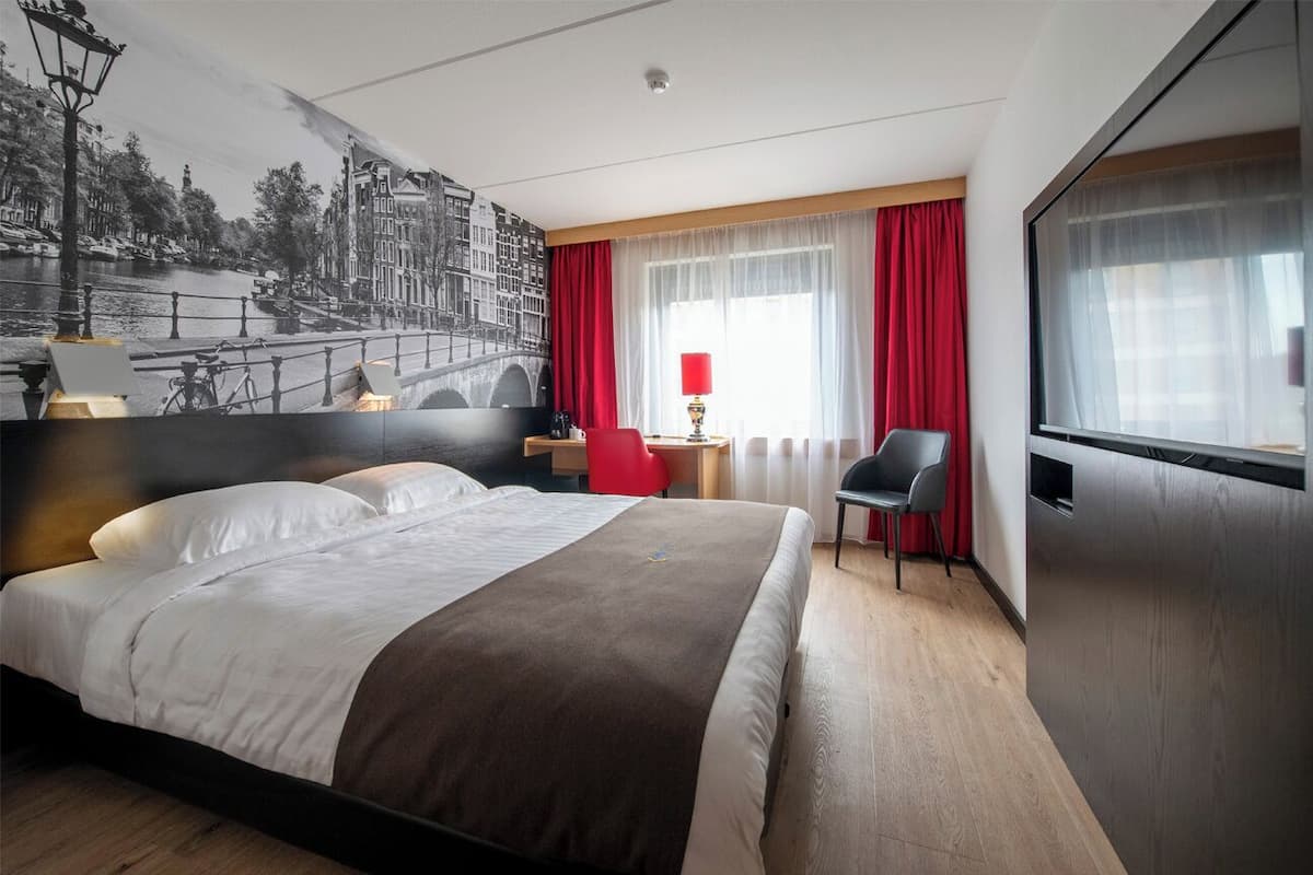 Habitación de hotel con una cama grande, un escritorio, una silla y un televisor.