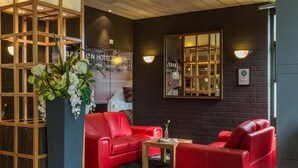 Een moderne hotel lobby met rode leren banken, een houten receptiebalie en een grote spiegel die de ruimte weerspiegelt.