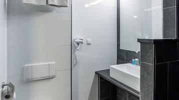 A modern bathroom with a white toilet, a glass shower enclosure, a vanity with a mirror, and a towel rack.