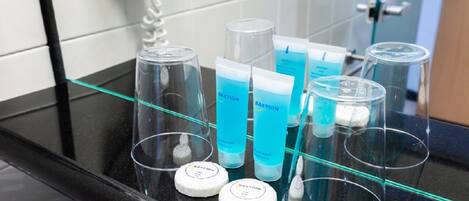 A bathroom counter with various toiletries including a hairdryer, a bottle of shampoo, and a tube of conditioner.