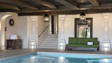 A pool area with a green sofa, a wooden cabinet, and a staircase leading to another level.