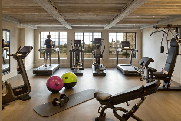 Un gimnasio con cintas de correr, elípticas y pesas libres, amplias ventanas con vistas y vigas de techo de madera.