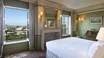A hotel room with a large bed, a fireplace, a view through a window, and a chandelier.