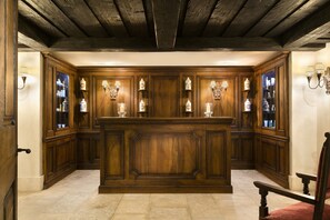 A traditional wooden interior with a central bar area, built-in shelves with glass doors, and wall-mounted lighting fixtures.