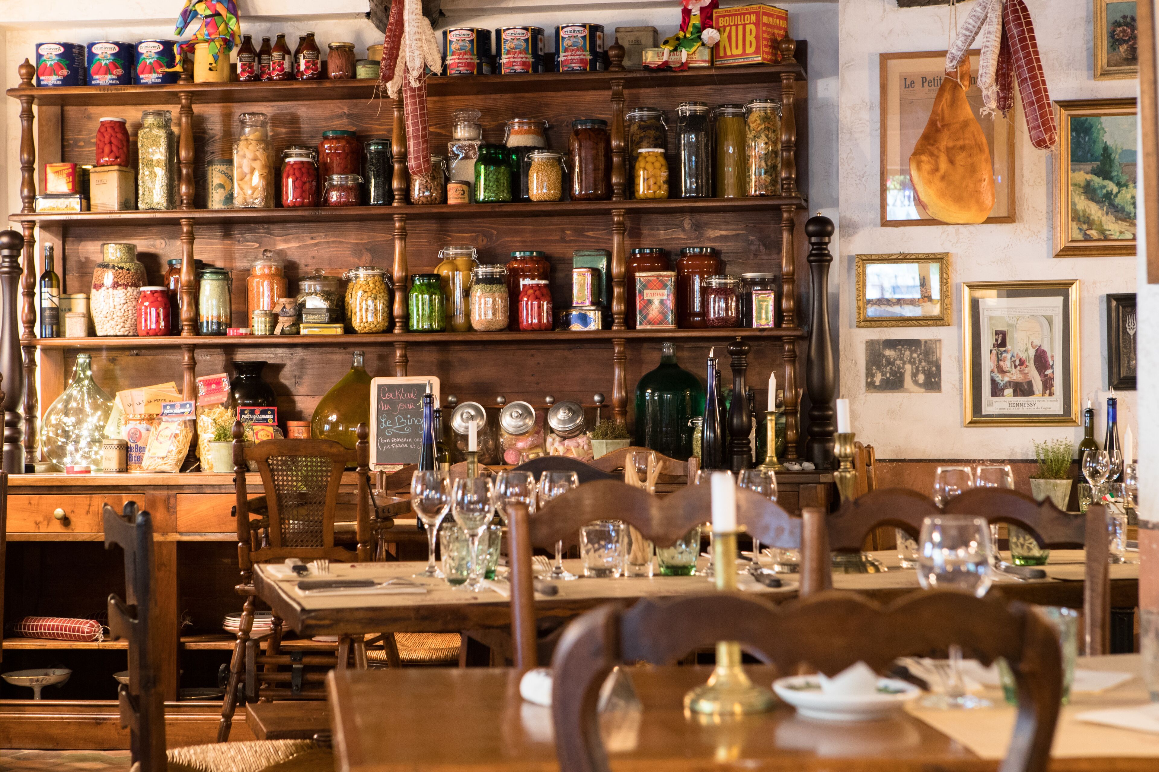 A dining area with wooden furniture, a variety of jars on shelves, and framed pictures on the wall.