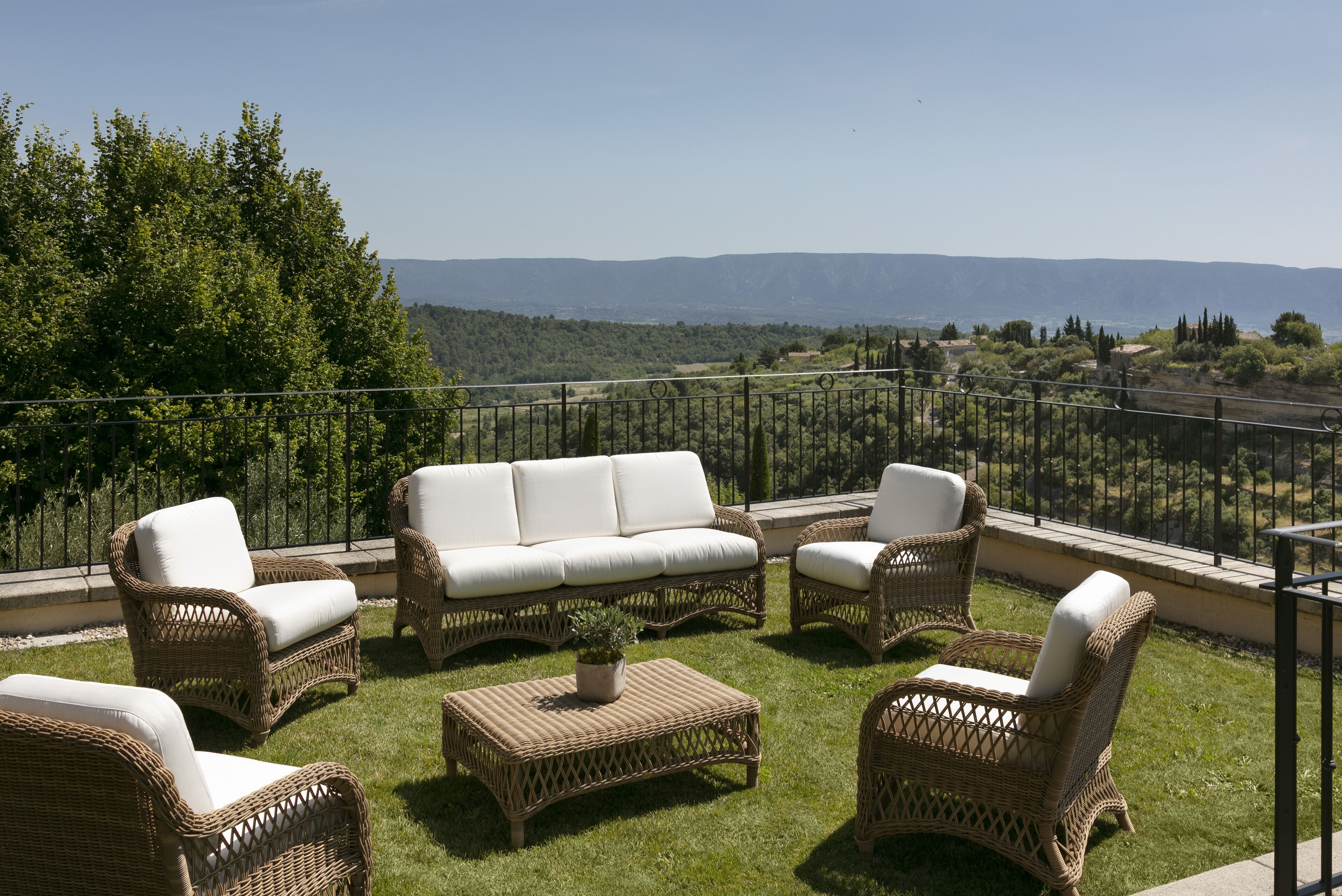 Une terrasse meublée de mobilier en osier, agrémentée d’une plante en pot, et offrant une vue sur des collines lointaines.