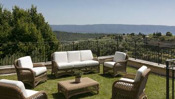 Une terrasse meublée de mobilier en osier, agrémentée d’une plante en pot, et offrant une vue sur des collines lointaines.