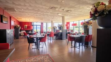 A spacious restaurant with red and black decor, multiple dining tables, and large windows providing natural light.