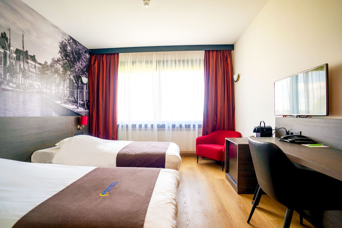 A hotel room with two beds, a desk, a chair, and a large window with curtains.