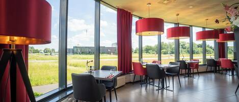 A modern restaurant with large windows, red curtains, and a view of a green field.
