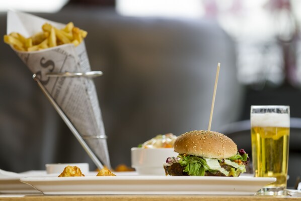 Una comida con una hamburguesa, papas fritas y una cerveza sobre una mesa.