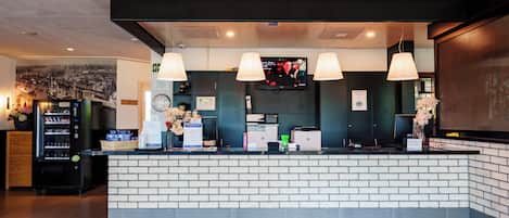 Una zona de recepción con mostrador de ladrillo, una pantalla digital y máquina expendedora.