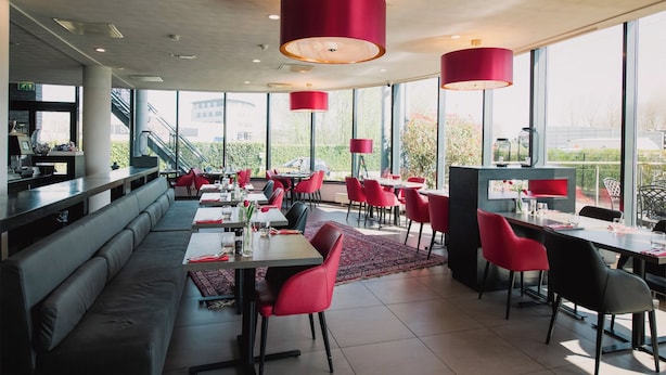 A modern restaurant with red chairs, large windows, and a view of the city.