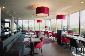 A modern restaurant with red chairs, large windows, and a view of the city.
