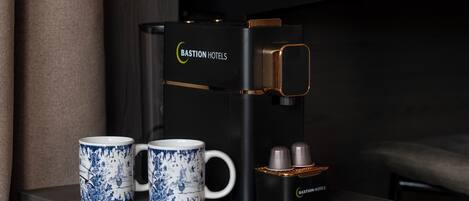 Una cafetera con diseño negro y dorado, dos tazas azules y blancas a juego, y un pequeño recipiente con dos copas plateadas.
