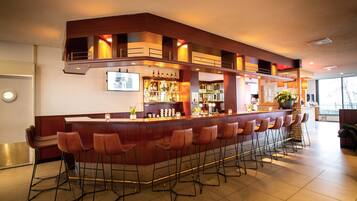A bar area with a long counter and multiple stools, a well-lit space with a modern design, and a visible bar stocked with bottles.
