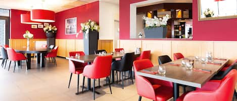 Un comedor moderno con sillas y mesas rojas, un espejo grande y una pared roja con un cartel.