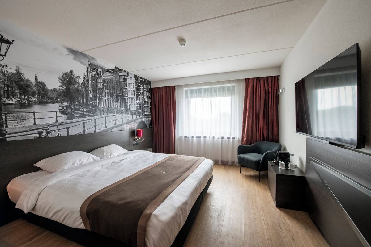 Ein modernes Hotelzimmer mit einem großen Bett, einem Flachbildfernseher, einem Schreibtisch und einem Sessel.