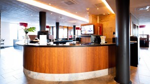 A modern reception area with a wooden reception desk, large pillars, and a flat-screen TV mounted on the wall.