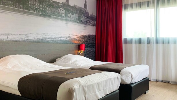 Ein Hotelzimmer mit zwei Betten, einem Stadtbild-Wandgemälde, einem roten Vorhang und einem Fenster mit leichtem Stoffvorhang.