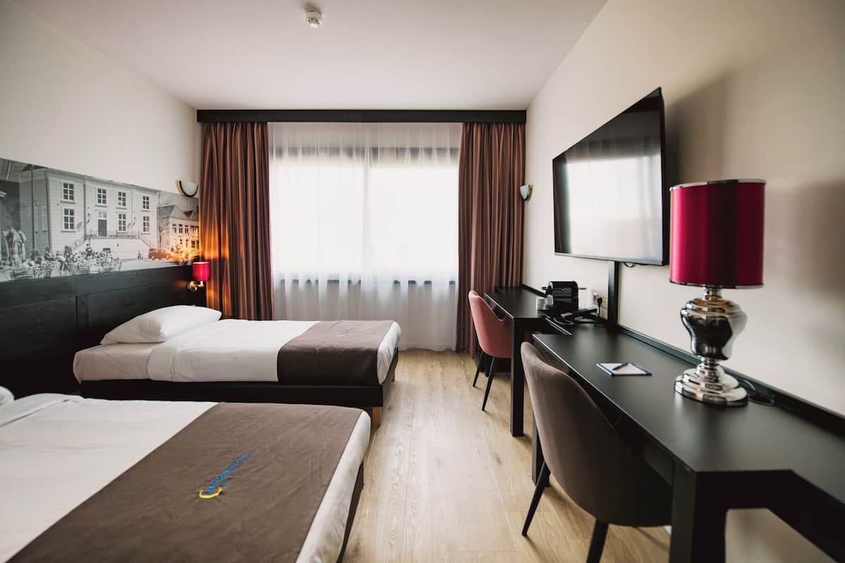 A hotel room with two beds, a desk with a computer, a TV, and a red lamp.