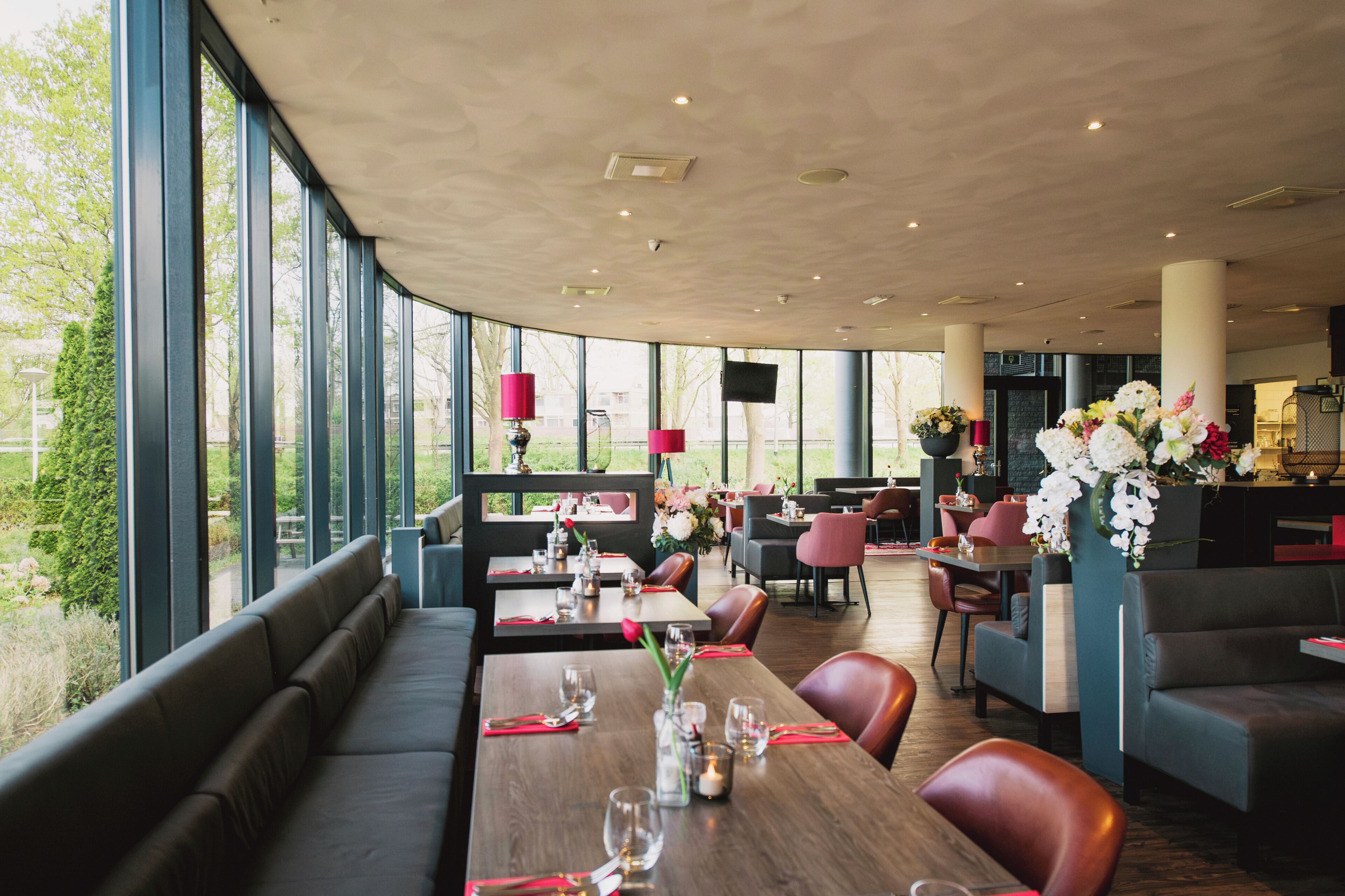Un restaurante con techos altos, amplias ventanas y diversas opciones de asientos, incluyendo cabinas y mesas.