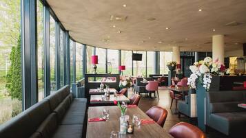 Un restaurante con techos altos, amplias ventanas y diversas opciones de asientos, incluyendo cabinas y mesas.