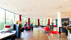 Un restaurante moderno con suelo de madera, sillas negras y rojas, y amplios ventanales que dan a zonas verdes.