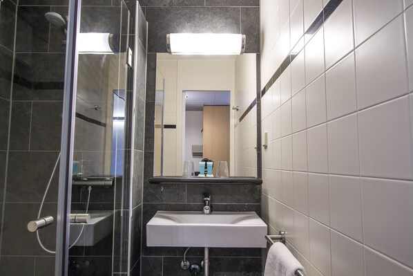 A modern bathroom with a glass-enclosed shower, a white sink, and a mirror above the sink. - Bastion Hotel Zoetermeer (Zoetermeer)