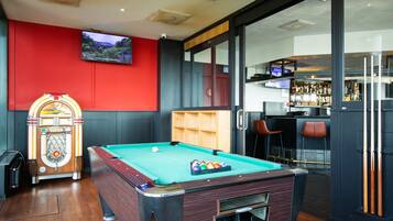 A pool table with a red wall and a bar area with stools.