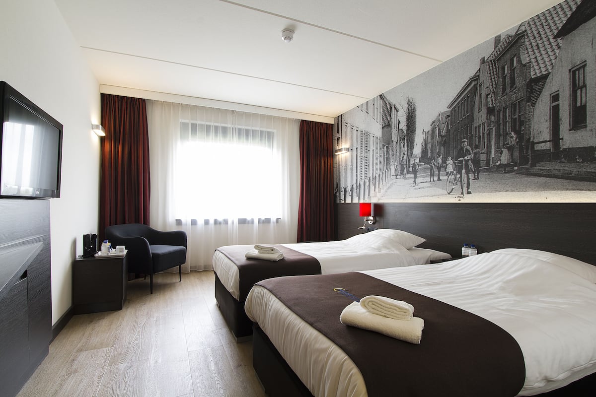 Une chambre d’hôtel avec deux lits, un téléviseur à écran plat, un bureau et une grande fenêtre avec des rideaux.