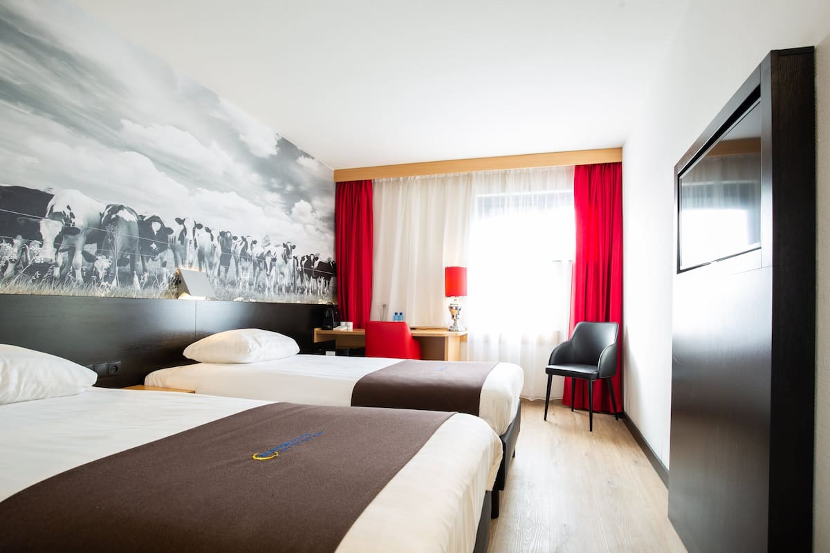 Une chambre d’hôtel avec deux lits, un bureau, une chaise, une télévision et une fresque murale.