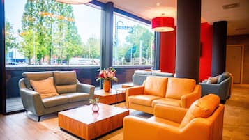 A modern lobby with leather sofas, a wooden coffee table, and large windows offering a view of trees and buildings.