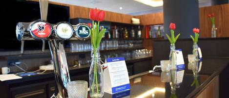 A bar area with taps labeled 'Jupiter' and 'Blonde'. There are vases with red flowers on the counter.